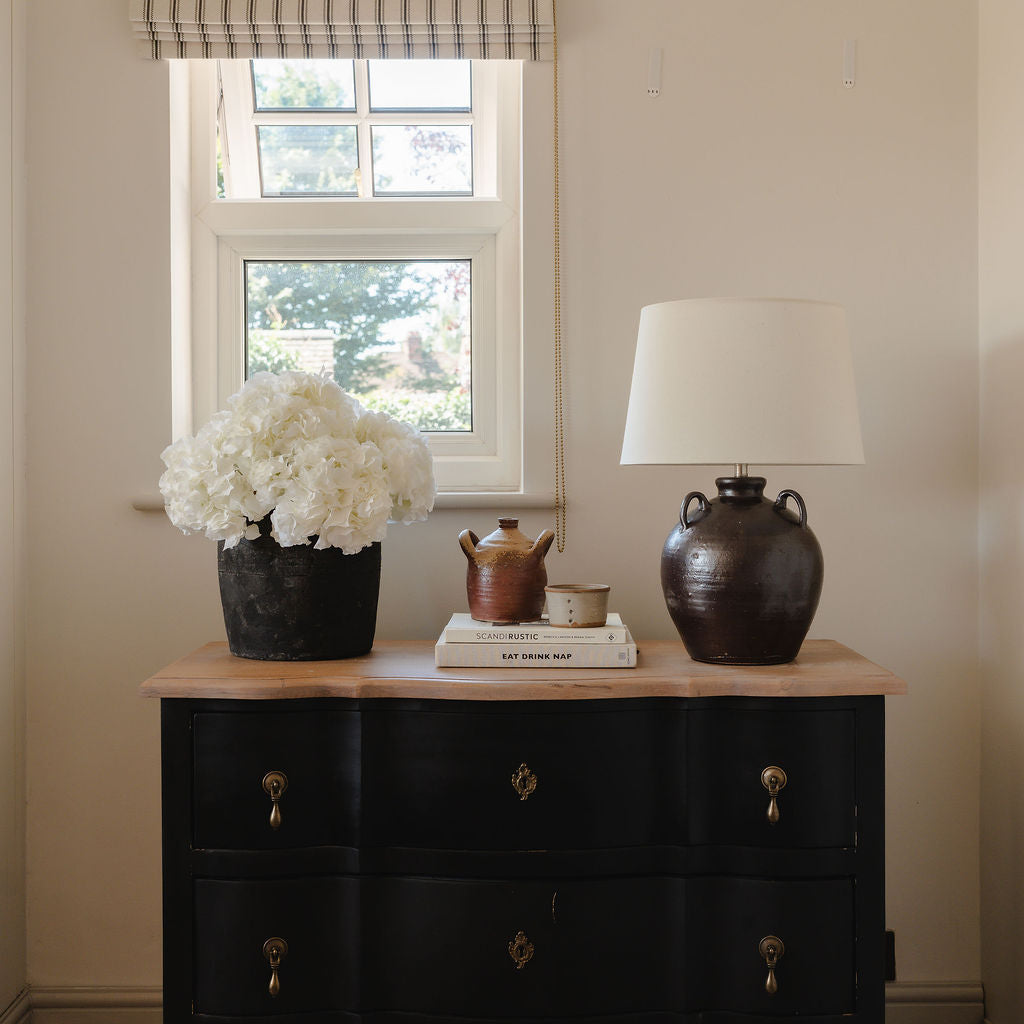 Black dresser with decorative items in a room with a window and lamp.