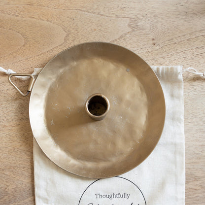 Brass lampshade on a branded cloth bag with 'Thoughtfully Handcrafted' logo on a wooden surface