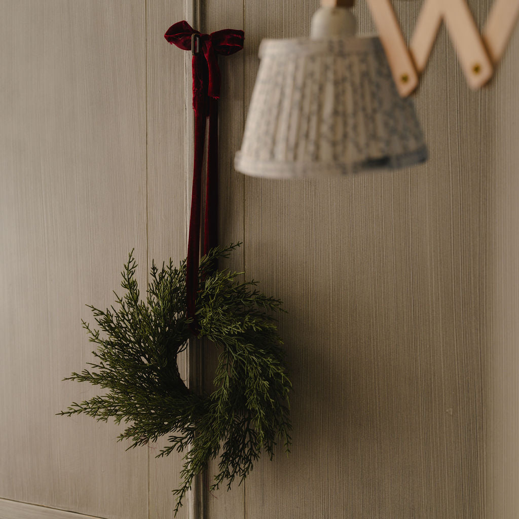 Decorative wreath with greenery and a red bow on a wooden door.
