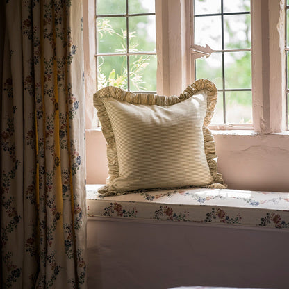 Decorative pillow on a window seat with floral curtains and a view of greenery outside.