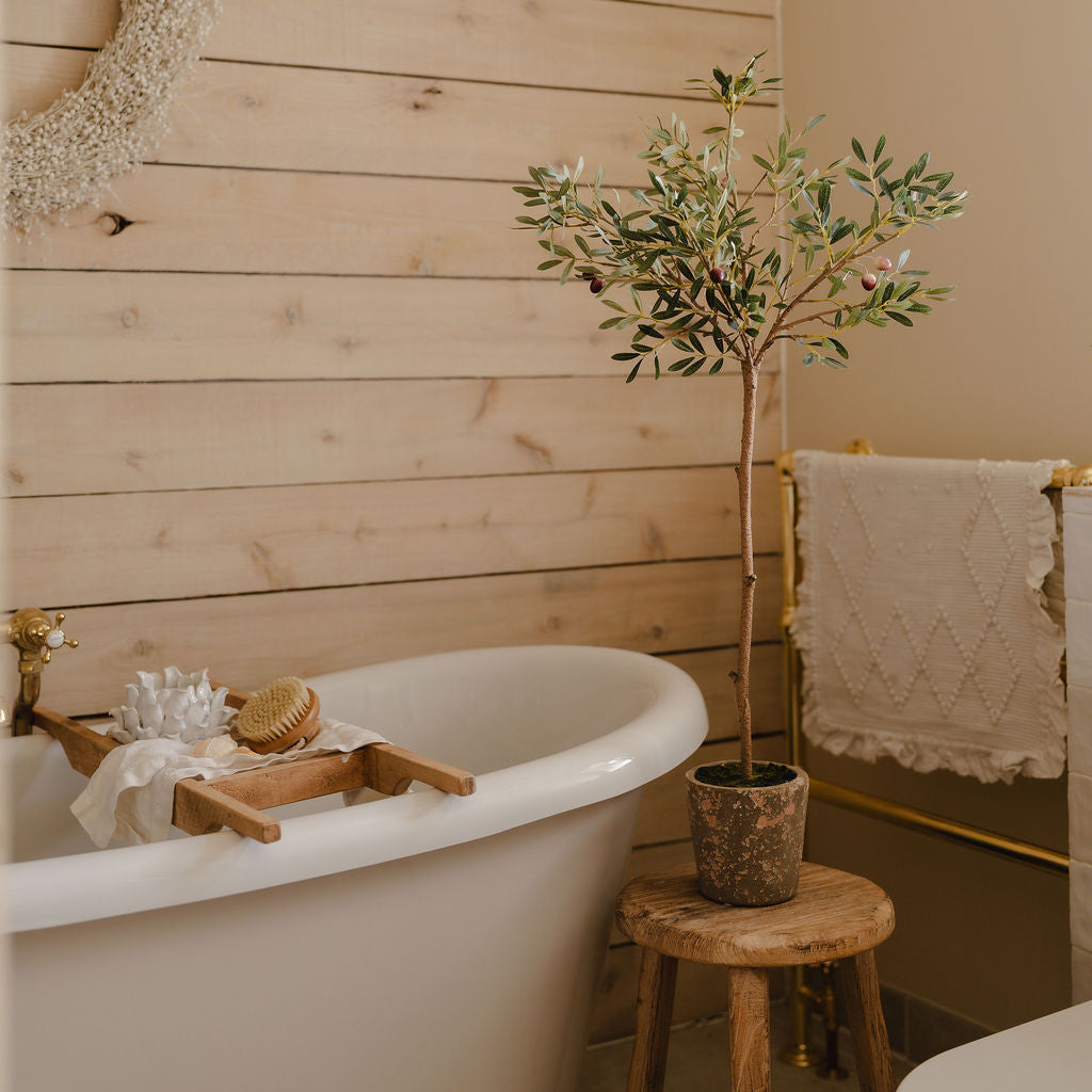 Bathroom with a freestanding bathtub, wooden stool, and potted plant.