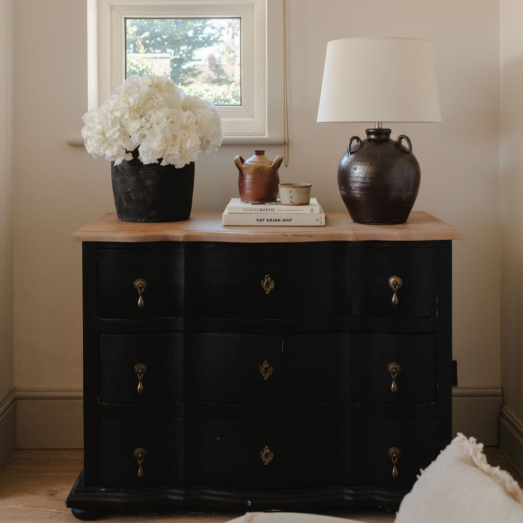 Black dresser with decorative items in a room with a window and lamp.