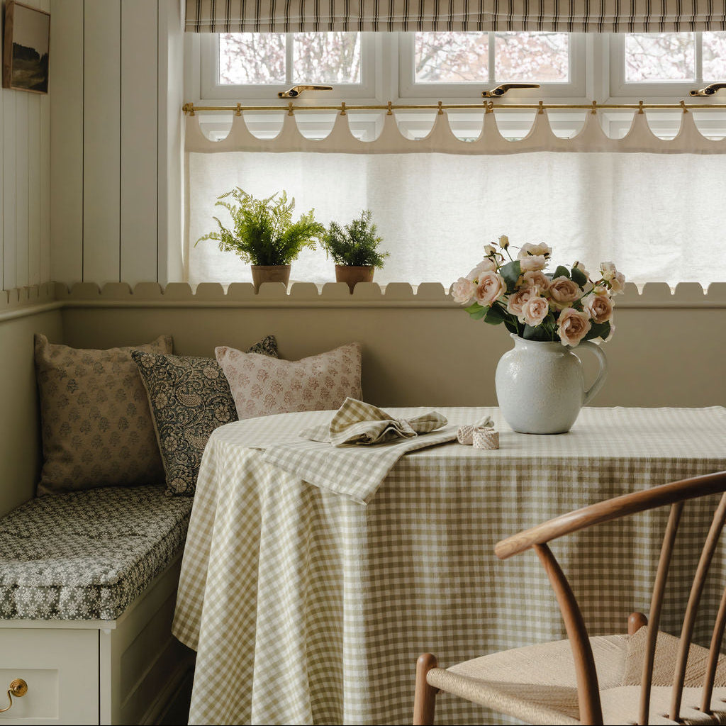 Nestled nook with a checkered tablecloth, cushioned bench, and floral arrangement.