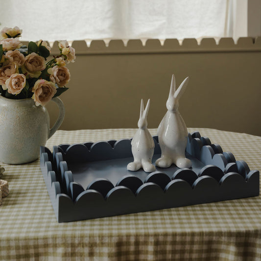 Two white rabbit figurines on a decorative tray with a vase of flowers in the background.