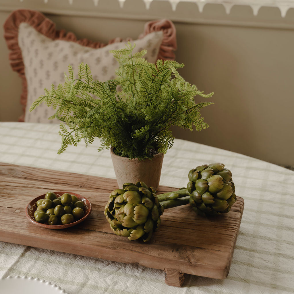 Decorative display of artichokes, a plant, and a small dish on a wooden board.