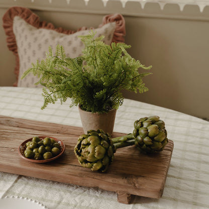 Decorative display of artichokes, a plant, and a small dish on a wooden board.