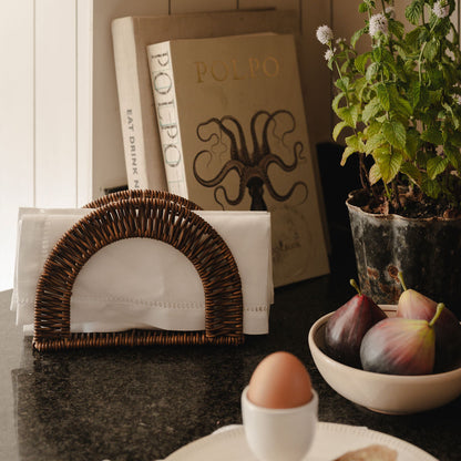 Napkin holder with white napkins, books, a plant, and a bowl of figs on a table.