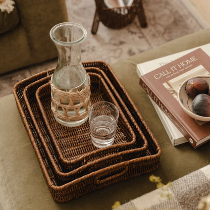 Wicker trays with a glass carafe and glass on a table with books and figs.