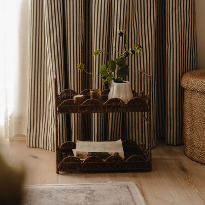 Wicker bar cart with decorative items against striped curtains