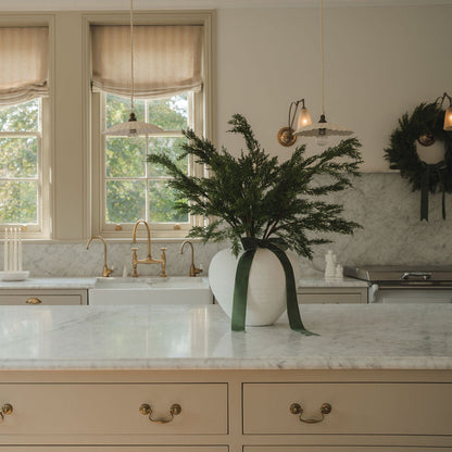 Decorative plant in a white vase on a kitchen counter with a wreath on the wall.