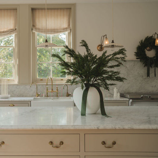 Decorative plant in a white vase on a kitchen counter with a wreath on the wall.