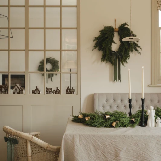 Dining room with a wreath on the wall, table with greenery, and candles.