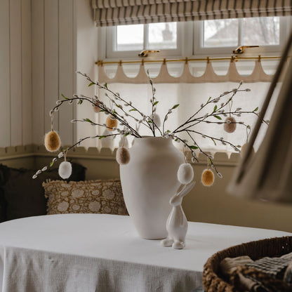 Decorative setup with a vase, branches, and small figurines on a table.