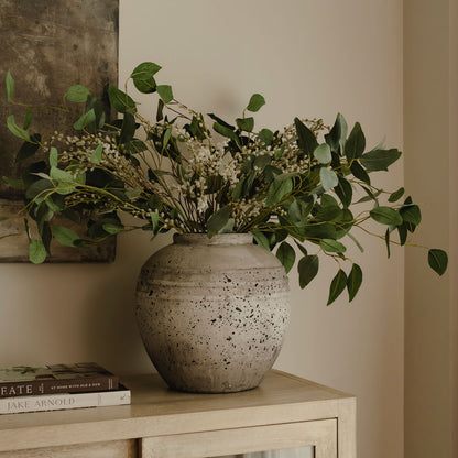 Decorative vase with greenery on a wooden surface against a neutral wall.