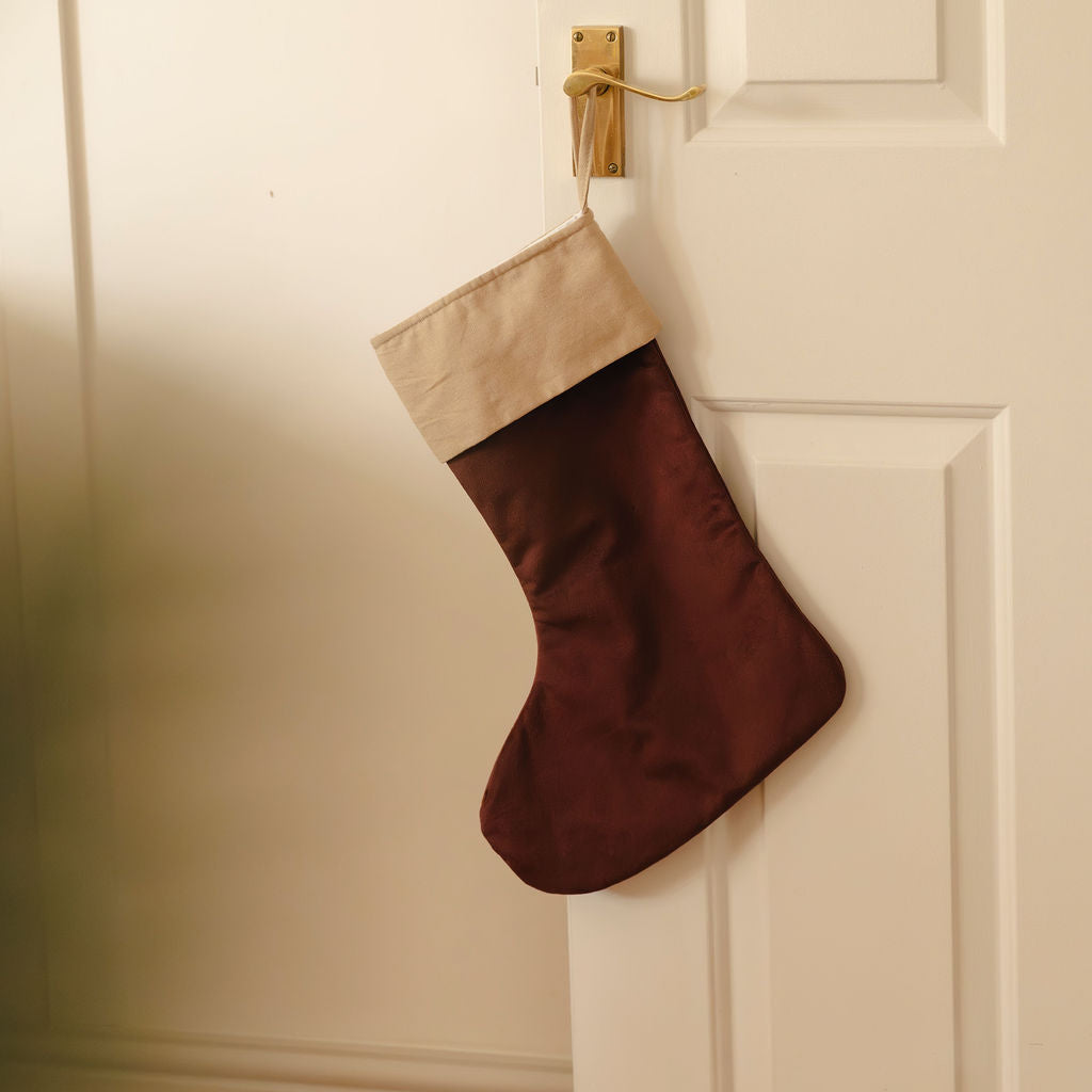 Burgundy Christmas stocking with cream top hanging on a white door.