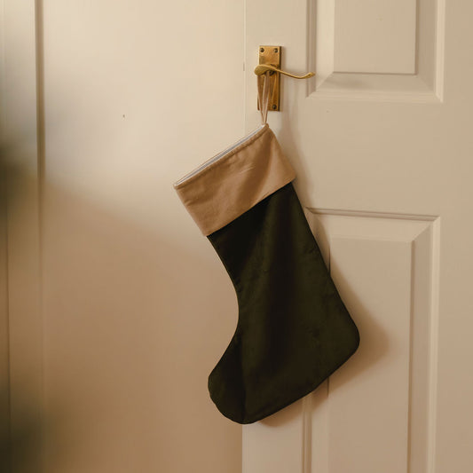 Green Christmas stocking with cream top hanging on a white door.