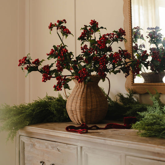 Decorative arrangement with red berries in a wicker vase on a wooden surface.